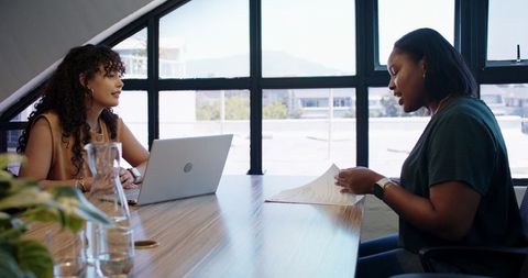 Two african american women collaborating in bright conference room reviewing documents