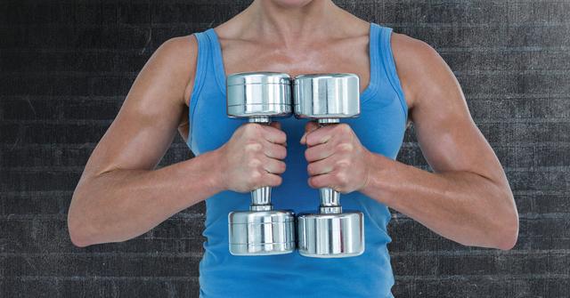 This image features a fit woman holding silver dumbbells against a dark textured background. Ideal for use in fitness blogs, workout manuals, gym promotions, and health lifestyle content, emphasizing strength training and physical fitness.