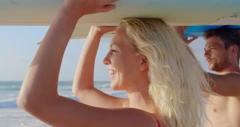 Smiling Couple Carrying Surfboard on a Sunny Beach