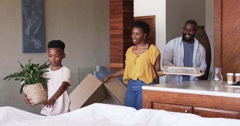 African American family unpacking in modern open-plan home with son carrying potted plant