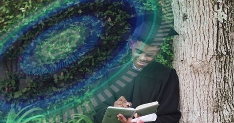 Graduate writing in notebook while leaning on tree with diploma and teal overlay