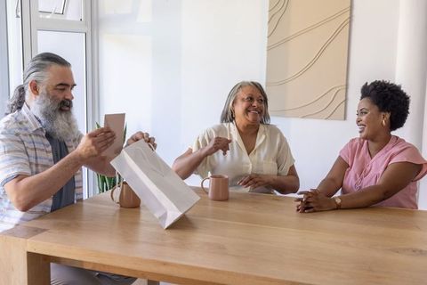 Multigenerational diverse family exchanging gift and card at sunlit wooden dining table