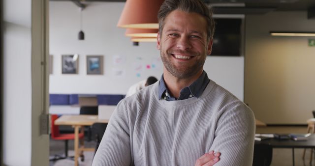 Businessman standing in a modern office with his arms crossed and a confident smile. Ideal for corporate websites, business blogs, professional success stories, and informational content about workplace culture or entrepreneurship.