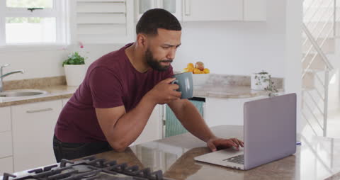 Man Enjoying Coffee Break While Browsing Laptop in Modern Kitchen