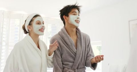 Couple enjoying morning skincare routine wearing face masks and plush robes