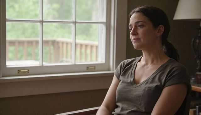 Contemplative middle-aged woman sitting by window gazing out at green backyard, home interior