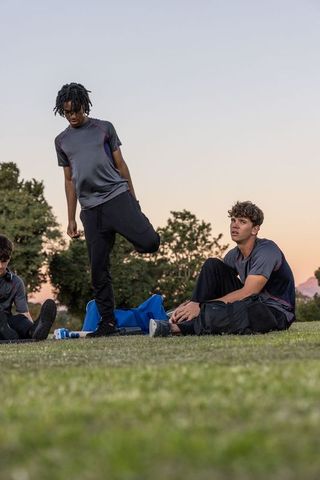 Diverse male athletes stretching and resting on grassy field at dusk with blue duffel