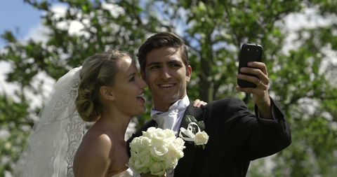 Joyful Newlyweds Taking Selfie Outdoors on Wedding Day