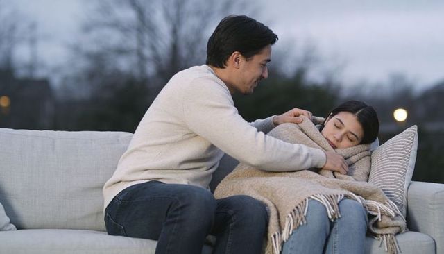 Man tucking blanket around sleeping woman on outdoor sofa at dusk showing tender care
