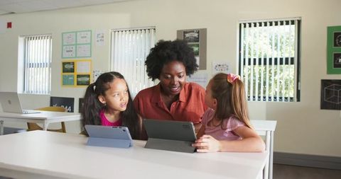 African American Teacher Guiding Two Girls with Tablets in Classroom for Digital Learning