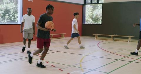 Young athletes dribbling basketball on indoor court during casual pickup game and training