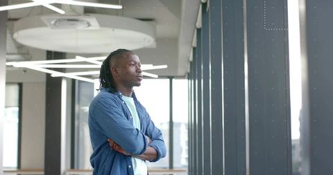 Young professional man standing gazing through floor-to-ceiling windows in modern office
