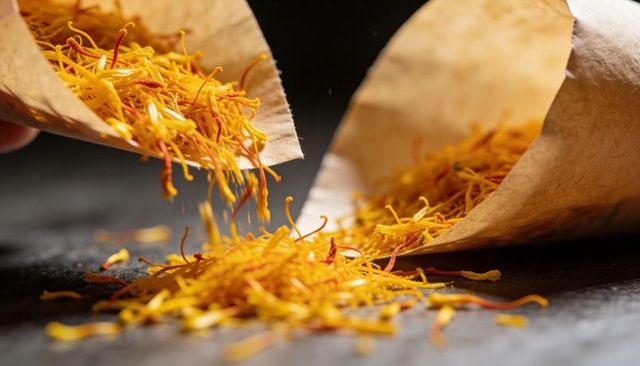 Pouring golden saffron threads from paper cones closeup, culinary spice macro