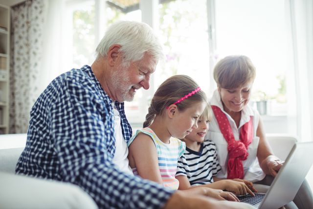 Grandparents and grandchildren sitting together on a couch, using a laptop. The scene captures a moment of bonding and learning, with the older generation teaching the younger one. Ideal for use in articles or advertisements about family, technology, education, and multigenerational relationships.