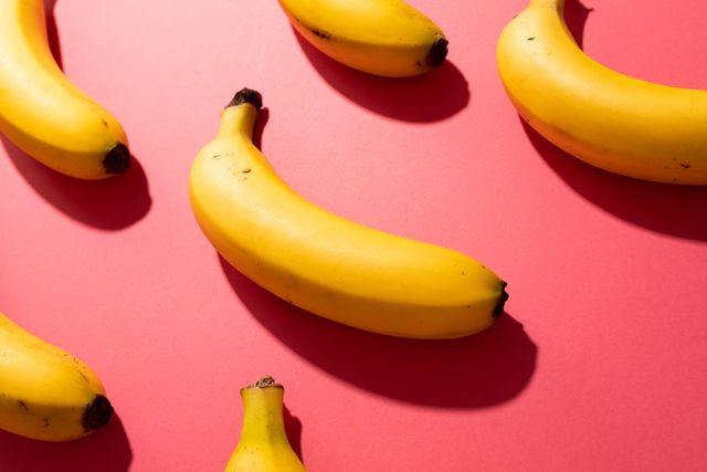 High angle view of fresh bananas arranged on a vibrant red background. Ideal for use in healthy eating promotions, organic food advertisements, and lifestyle blogs. The bright colors and simple composition make it perfect for social media posts, website banners, and print materials.
