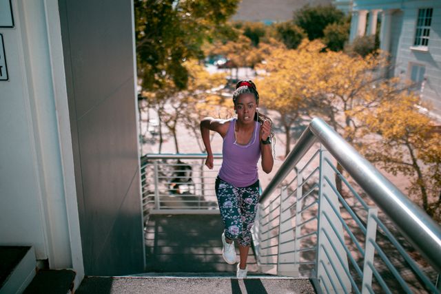 African American woman running up stairs in urban environment at sunset, showcasing determination and fitness. Ideal for promoting healthy lifestyles, fitness programs, outdoor activities, and urban exercise routines.
