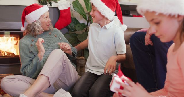 Family enjoying Christmas together by the warm fireplace, wearing Santa hats and sharing gifts. Perfect for holiday season promotions, family-oriented advertisements, and festive greeting cards expressing joy and family bonding.