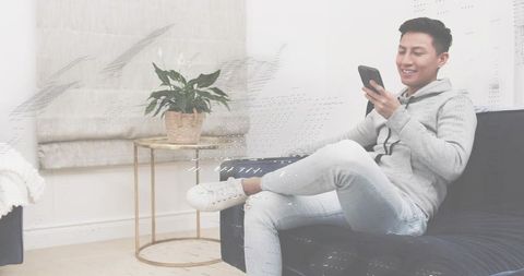 Young man relaxing on sofa browsing smartphone in minimalist living room