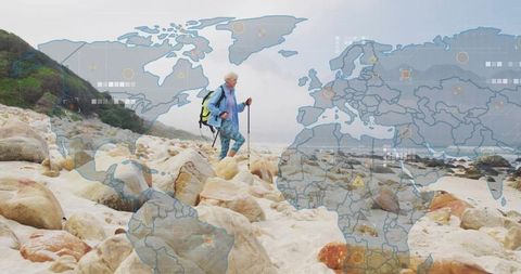 Senior woman hiking rocky coastline with trekking pole and world map data overlay