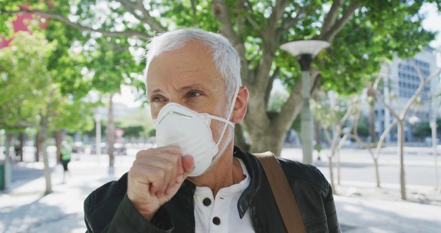 Mature man wearing a mask and coughing outdoors, emphasizing health safety during pandemic and polluted environments. Ideal for use in articles on healthcare, virus protection, seniors' health, and public awareness about pollution and COVID-19 precautions.