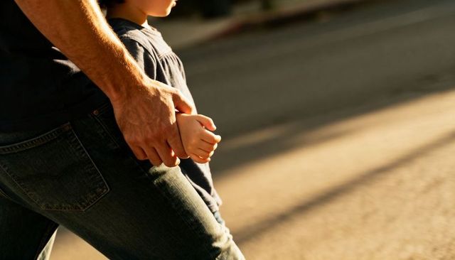 Father and child walking holding hands on sunlit sidewalk with warm golden light and long shadows