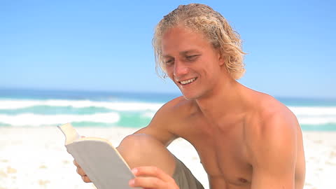 Man Enjoying Novel while Relaxing on Sunny Beach
