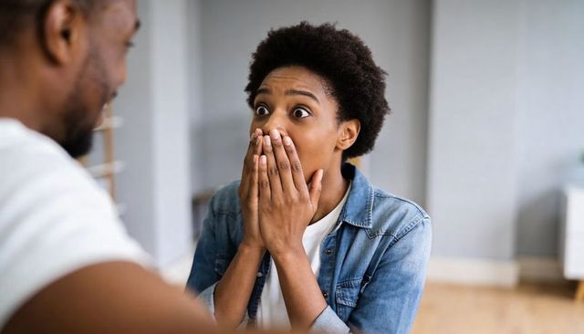 Surprised black woman covering mouth with hands reacting to unexpected news in living room