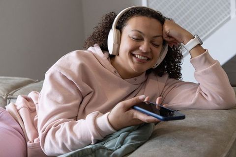 African american woman relaxing on couch listening to music with headphones and smartphone