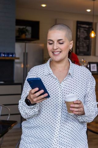 Smiling woman checking phone while holding coffee in modern cafe — casual work lifestyle