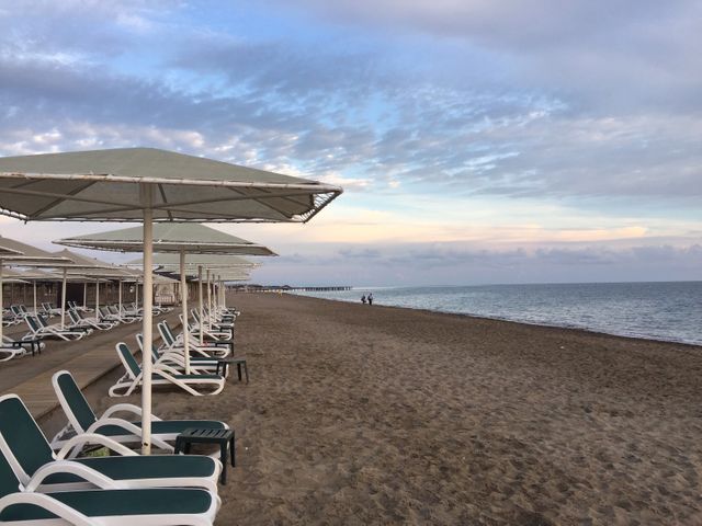 Beach with neatly arranged sun loungers and umbrellas. Ready for visitors during sunset. Peaceful atmosphere ideal for promoting vacation spots, travel blogs, or stress-relief content. Showcasing quiet coastal destinations or resorts emphasizing relaxing environments.