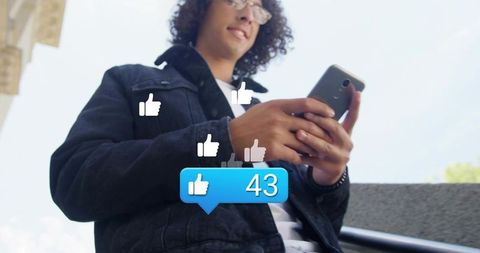 Young man holding smartphone on urban stairs getting social media likes and notifications