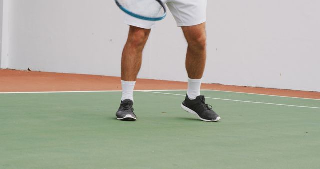 Man playing tennis in black sneakers and white shorts on an outdoor court. Useful for promoting active lifestyles, sportswear, tennis events, training programs, and fitness brands.