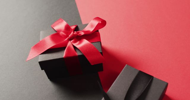 Close up of two black gift boxes with red and black ribbons on black and red with copy space. Luxury treat, present, shopping, black friday sale and retail concept digitally generated image.