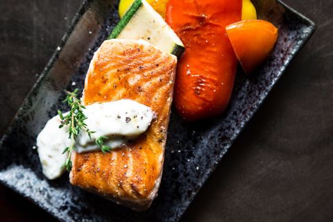 Pan-searing salmon fillet with creamy herb sauce and roasted peppers on black plate