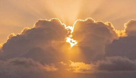 Golden sunbeams casting through backlit cumulus cloud bank at sunrise