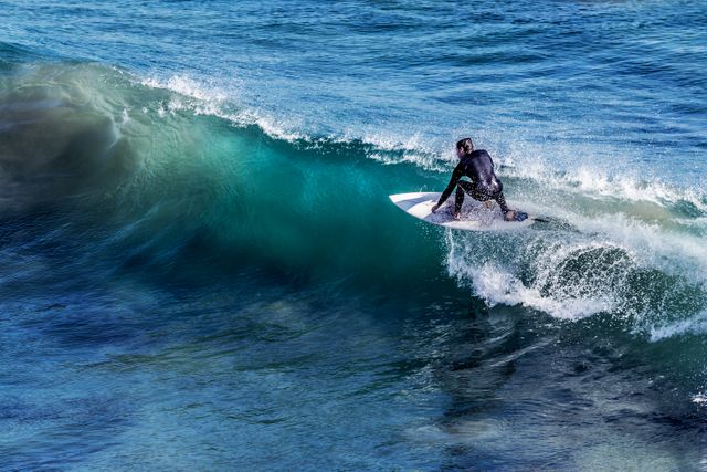 Surfer riding wave on clear blue ocean water. Perfect for use in travel brochures, sports advertisements, summer campaigns, and outdoor lifestyle content depicting adventure and aquatic activities.