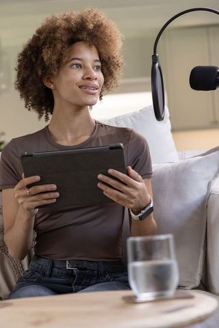 African american woman recording podcast at home holding tablet with microphone