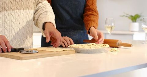 Couple Preparing Lattice Pie Together on White Counter With Rolling Pin and Wine Glasses