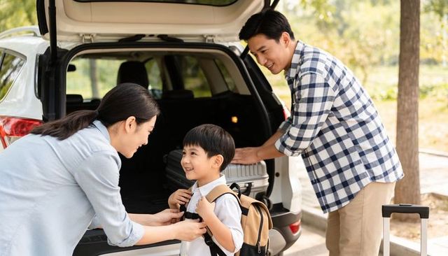 Family packing for road trip parents loading luggage and fastening child backpack by car