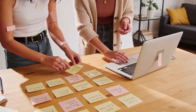 Two women collaborating with sticky notes and laptop in cozy minimalist home workspace
