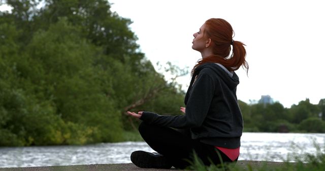 Woman practicing meditation by a riverside, emphasizing the importance of calmness and connection with nature. Ideal for stress relief, wellness, mindfulness, and mental health promotions, or for illustrating concepts related to yoga and outdoor activities.