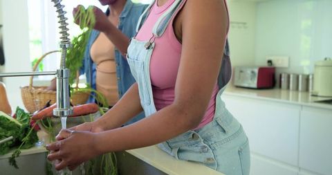 African mother and daughter washing fresh vegetables at bright kitchen sink