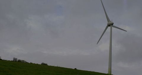 Solitary wind turbine on green hillside under overcast skies