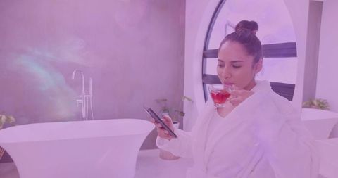 Indian woman holding teacup and checking smartphone while relaxing in luxury bathroom