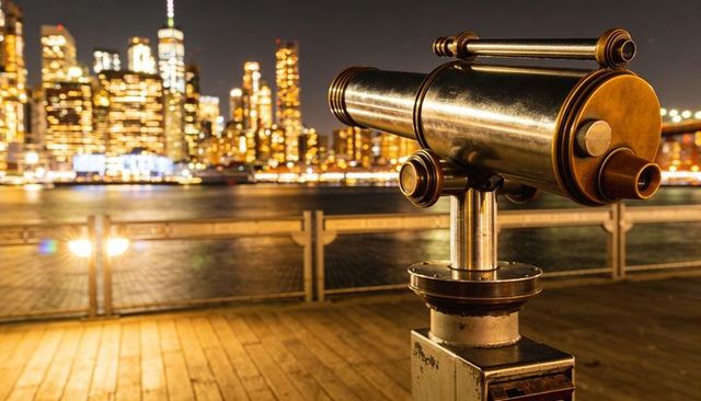 Brass coin-operated viewer on waterfront pier with bokeh city lights and river reflections
