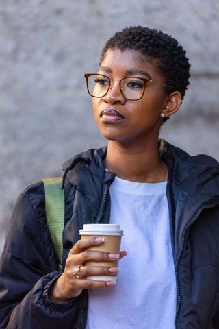 Thoughtful african american woman holding coffee wearing glasses and puffer jacket