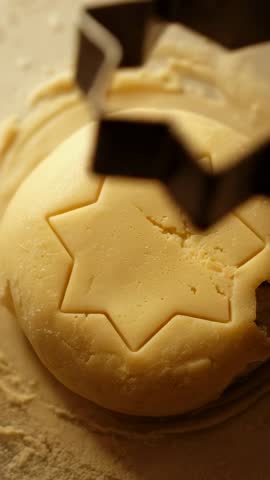Vertical close-up of star cookie cutter pressing and shaping soft dough for baking