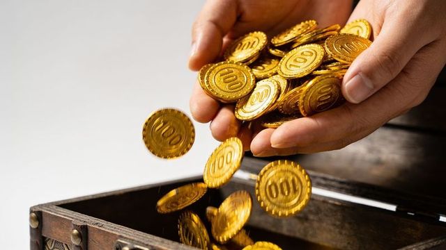 Hands pouring shiny 100 coins into ornate wooden chest conveying wealth, savings, reward