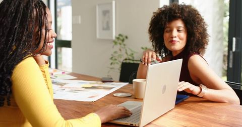 Collaborating women smiling while working on laptop and moodboard in bright modern home office