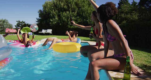 Diverse group of friends having fun playing on inflatables in swimming pool. hanging out and relaxing outdoors in summer.